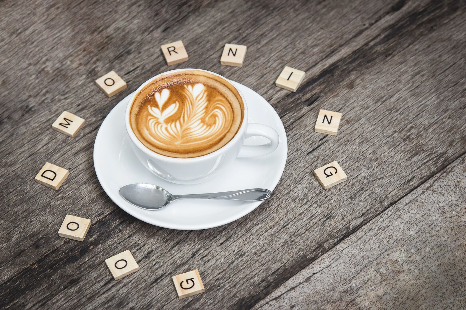 Home Cup of cappuccino with latte art surrounded by Scrabble letters spelling 'Good Morning'.
